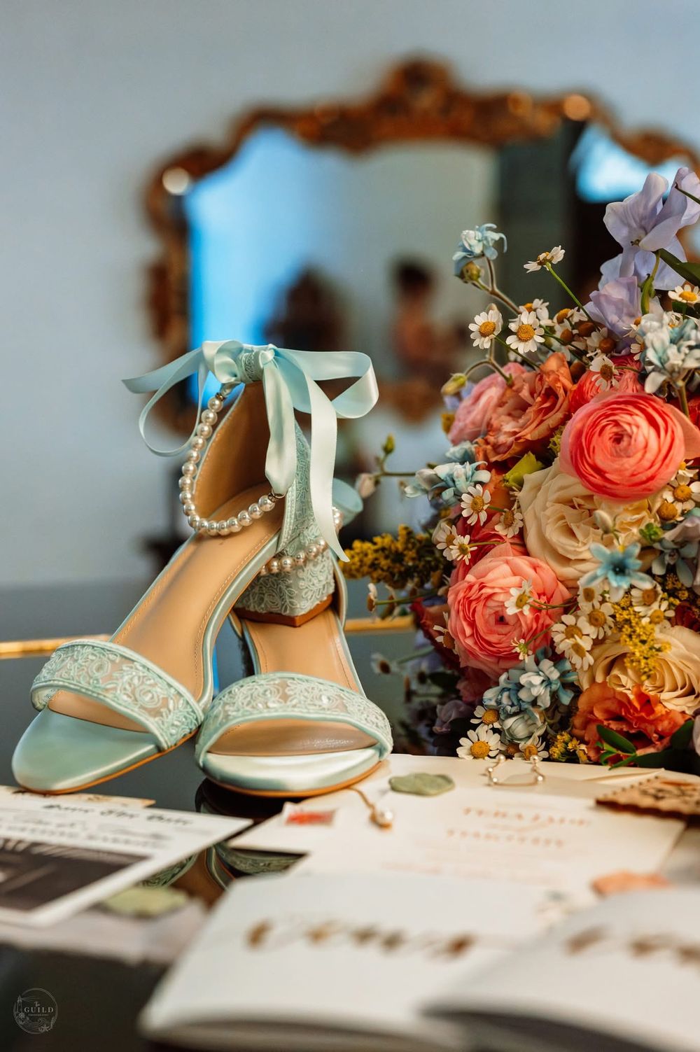 Light blue pearl-embellished bridal heels with ribbon ties displayed beside a colorful floral bouquet.