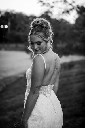 A bride in a backless lace gown looks down gracefully in a black and white outdoor portrait.