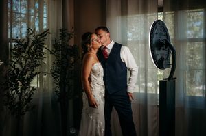 Bride and groom sharing a romantic kiss at their wedding reception, with elegant drapes and soft lighting in the background.