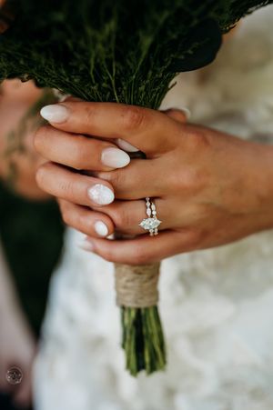 Close-up of a bride holding a greenery bouquet, showcasing a marquise diamond engagement ring with a delicate diamond band.