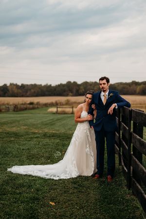 Bride and groom posing by a rustic wooden fence in a green field during their outdoor fall wedding.