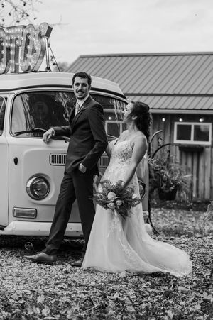 Black and white photo of bride and groom standing by a vintage VW bus at their fall wedding.