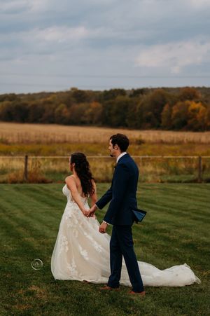 Bride and groom holding hands while walking through a scenic autumn field at their fall wedding.