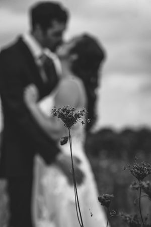 Romantic black and white photo of bride and groom kissing in a meadow with wildflowers in foreground.