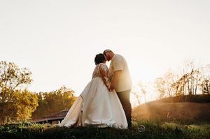 Bride and groom share a romantic sunset kiss on a grassy hill at their outdoor wedding ceremony.