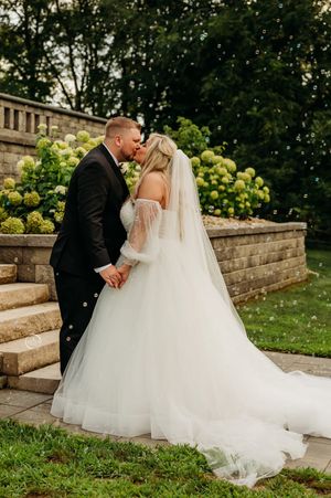 Bride and groom kiss on stone steps surrounded by blooming hydrangeas with bubbles floating around them.