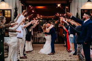 Bride and groom kissing under sparklers held by wedding guests during romantic outdoor sparkler send-off celebration.
