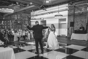 A bride and groom share their first dance on a black and white checkered floor in an industrial venue.