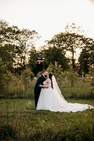 A bride and groom share a romantic kiss in a lush green meadow during a golden hour sunset wedding.