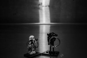 Black and white photo of two figurines facing each other with dramatic light beam in background.