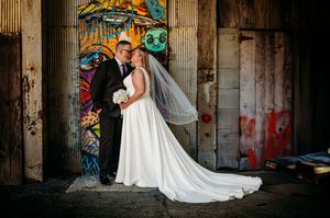 A bride and groom share a romantic moment in front of colorful graffiti doors in an urban wedding setting.