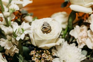 Wedding rings resting on a white rose surrounded by elegant floral arrangements.