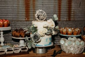 Two-tier wedding cake with Mr & Mrs topper surrounded by roses and greenery on dessert table.