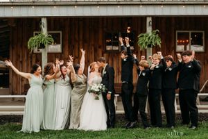 Joyful wedding party celebrating in front of rustic wooden barn venue.