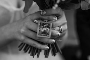 Black and white close-up of bride holding bouquet with small memorial photo charm.