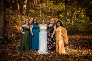 Bride with four bridesmaids in colorful dresses posing among fall foliage in an outdoor woodland setting.