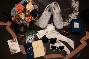 A flat lay of wedding details including a colorful bouquet, pearl sneakers, invitation suite, and accessories.