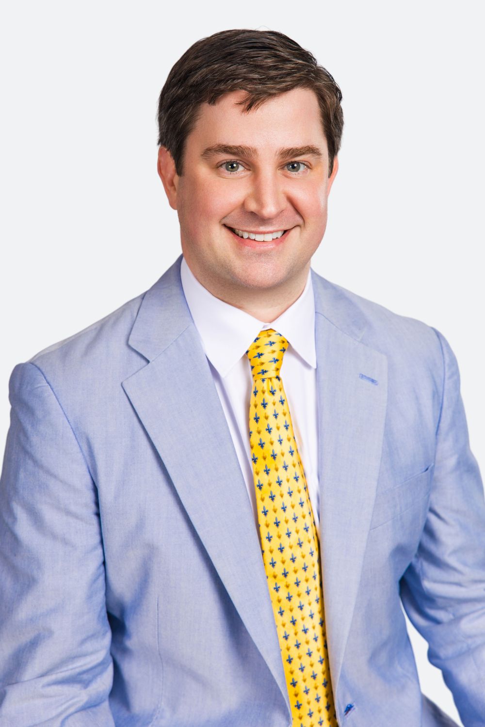Professional man in light blue suit and yellow patterned tie smiling for a corporate headshot photo.