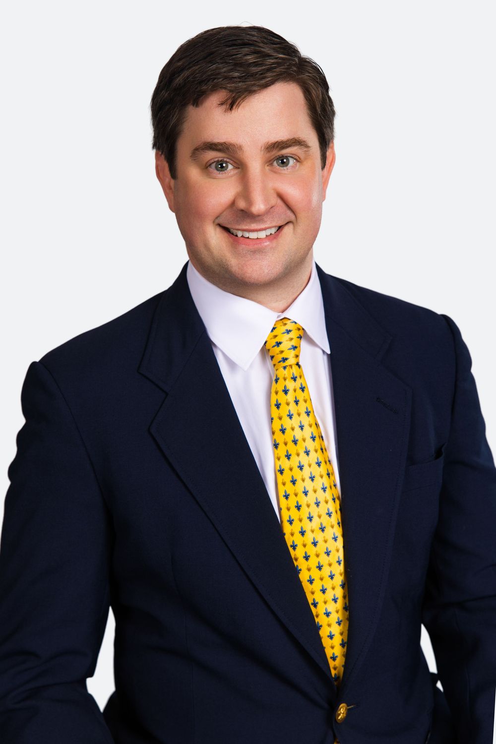 Smiling businessman in navy suit and yellow patterned tie poses for professional headshot photo.