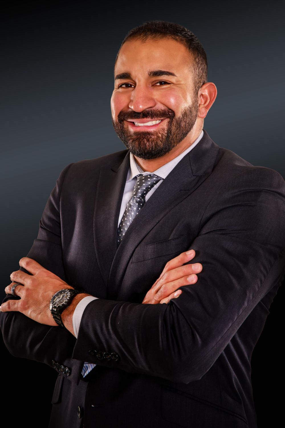 Professional studio portrait with crossed arms wearing dark suit and patterned tie.