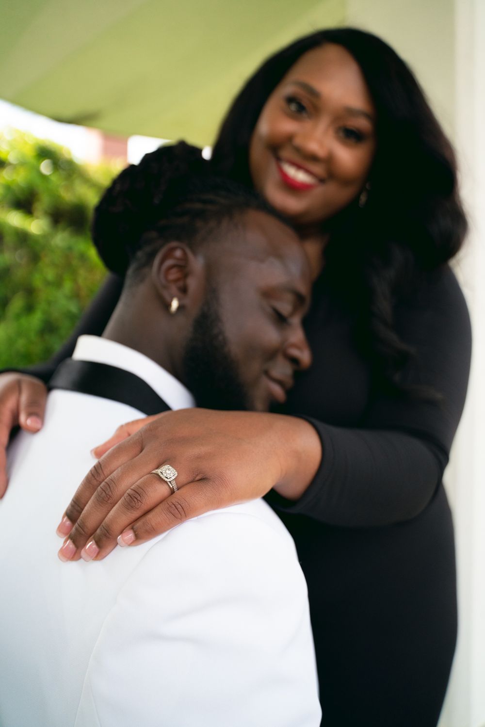 A tender embrace between a couple showing a close-up of an engagement ring on display.