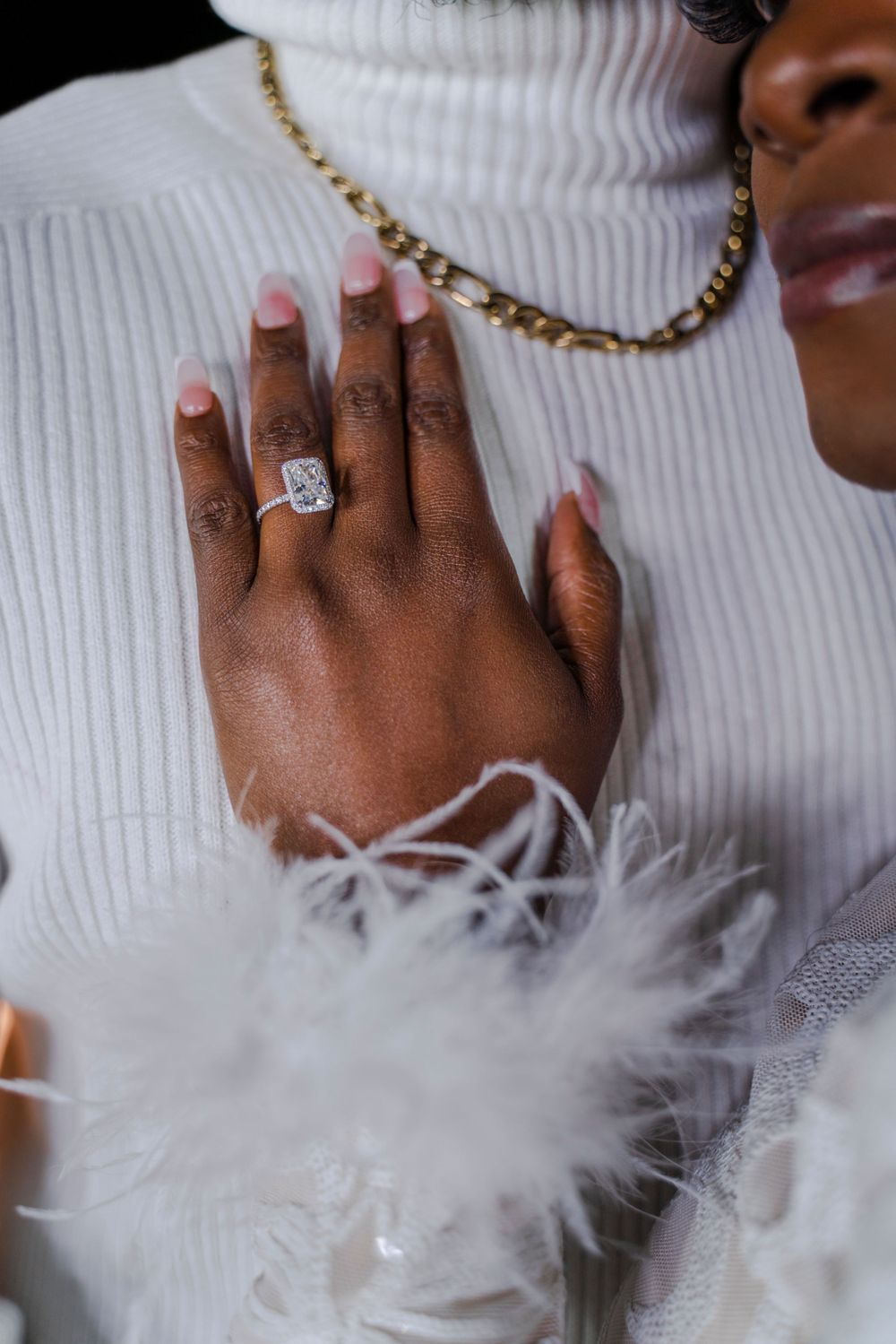 Close-up of an elegant diamond engagement ring on a hand adorned with a gold chain necklace.