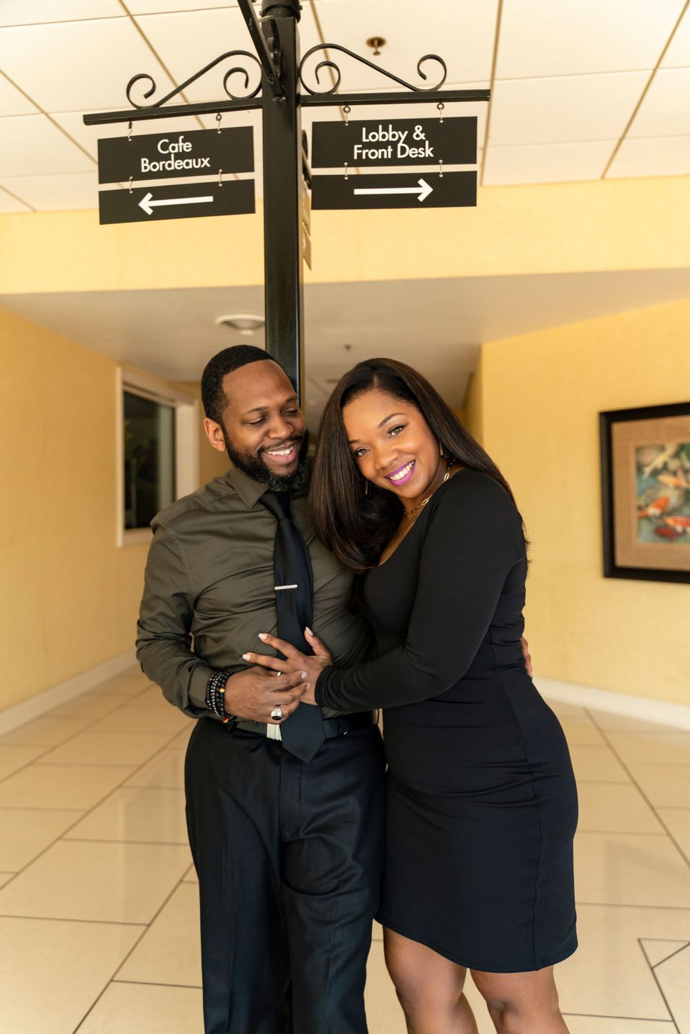 A happy couple shares an intimate moment under directional signs in a bright indoor hallway.