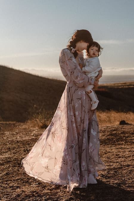 Ethereal sunset portrait of figures in a flowing mauve dress against a golden hillside landscape.