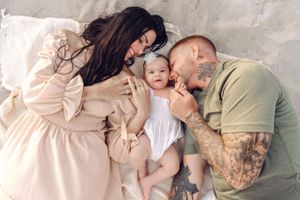 Intimate family moment on white bedding with baby in center.