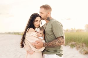 Family embracing on beach with soft sunset lighting and coastal scenery.