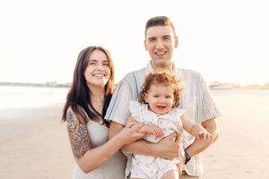 Happy family portrait on beach with warm sunset lighting in background.