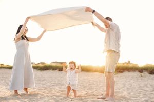 Family playing together on a sandy beach during golden hour sunset.