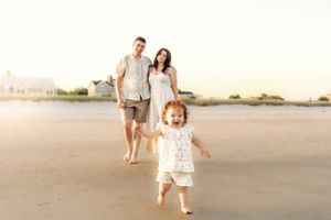 Family walking and playing together on a beach at sunset with soft lighting.