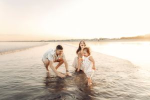 Family splashing and playing in ocean waves during sunset.