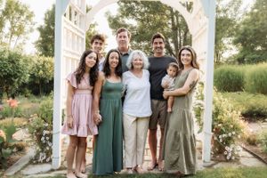 Family group poses together in a garden setting with white arbor and summer greenery.