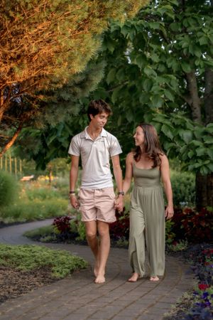 Couple walking barefoot together on a garden path during golden hour.