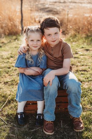 Two children sitting together on wooden bench during sunset outdoor photo session.