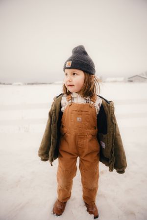 Small child wearing brown Carhartt overalls and winter hat plays in the snow.
