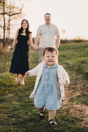 Toddler in denim dress running happily through field at sunset.