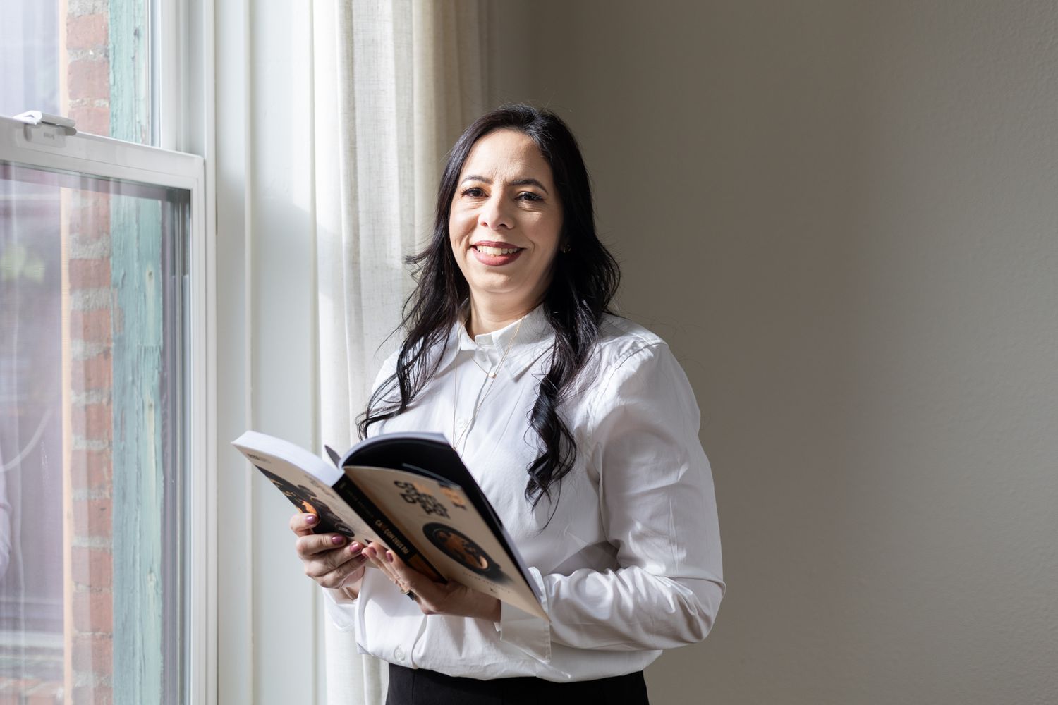 Person reading by a window in professional attire with natural light streaming in.