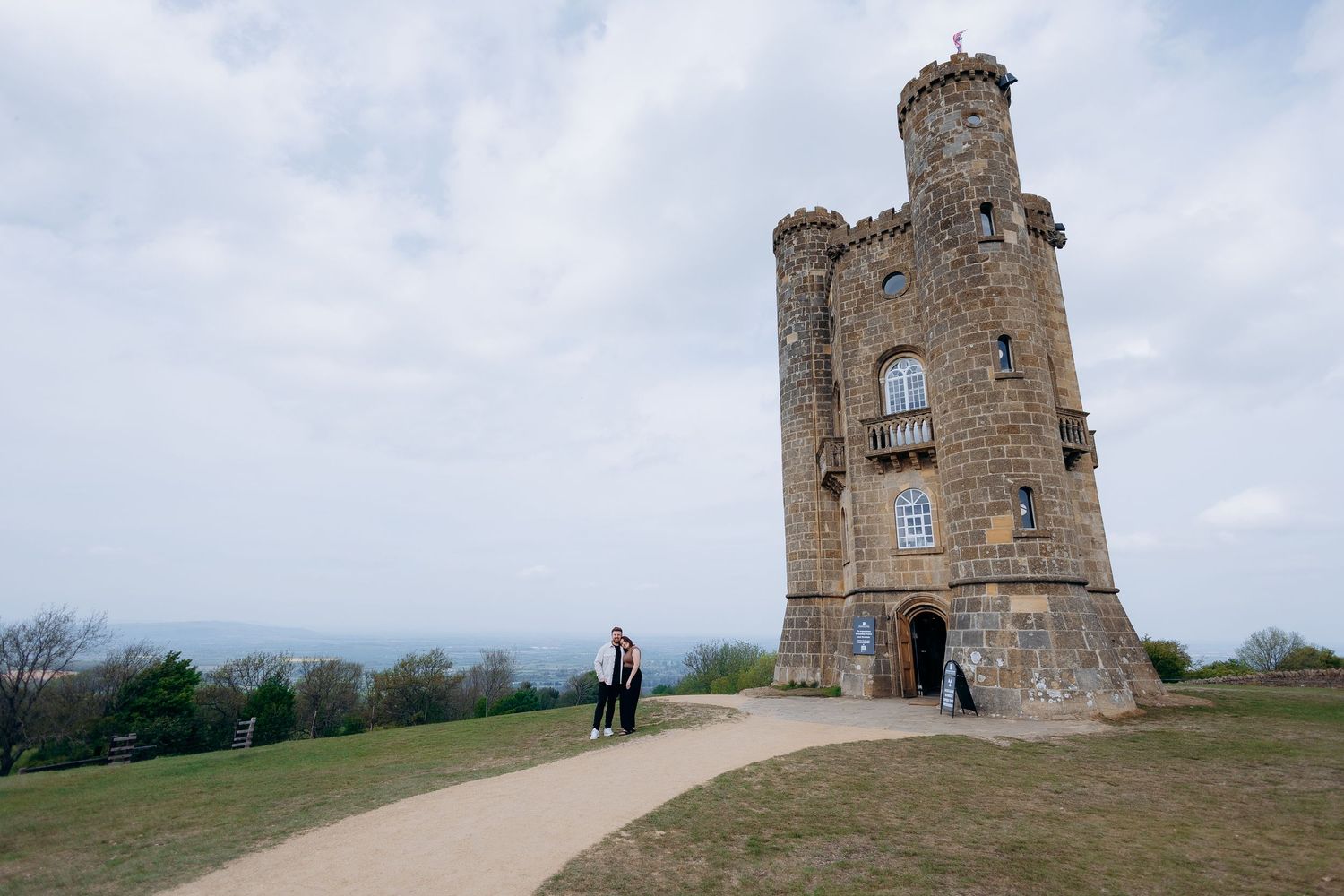 Couples posing near Broadway Tower, a historic folly castle on a hilltop in the Cotswolds, England.