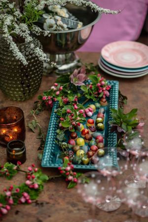 Colorful fruit and floral display on a turquoise platter with wine glasses and candlelight.