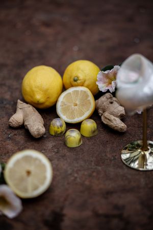 Fresh lemons, ginger root, and small green olives arranged on a rustic surface with glassware.