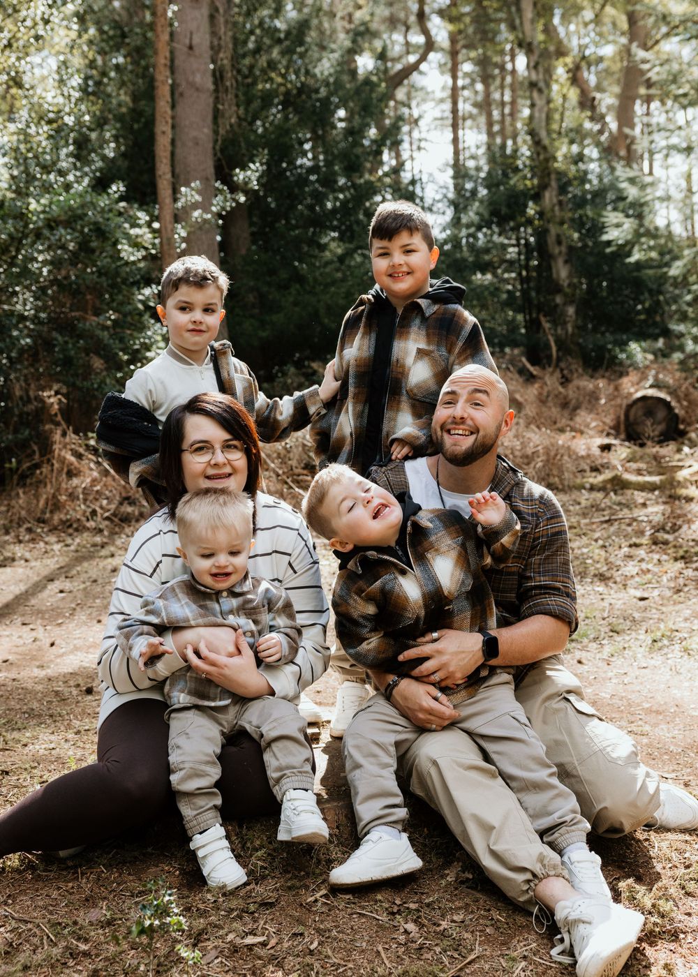 A happy family of five poses outdoors in a forest setting, wearing casual flannel and striped outfits.