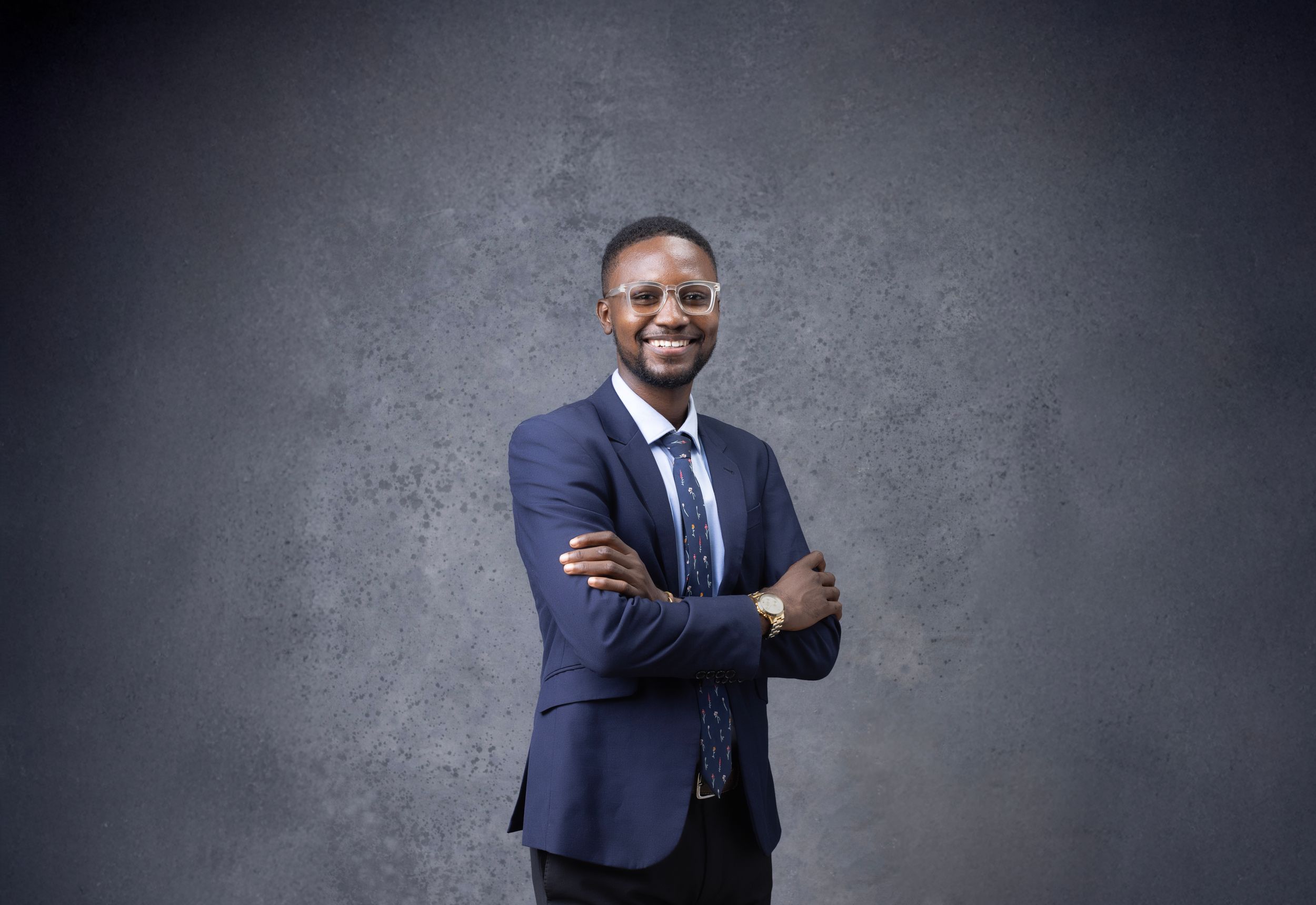 Professional portrait of someone in navy suit against textured grey background.