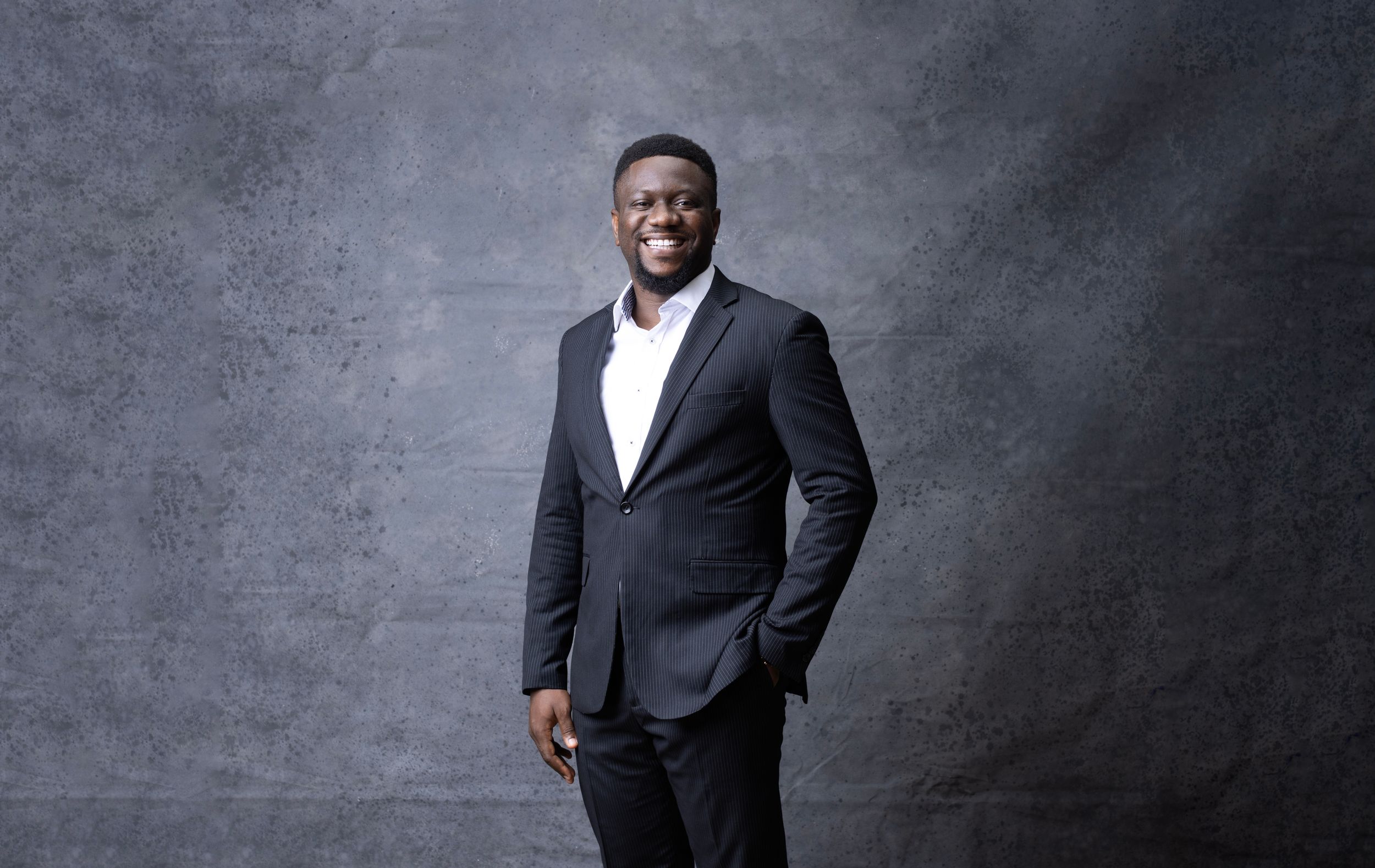 Professional studio portrait of person in pinstriped suit jacket against textured gray background.