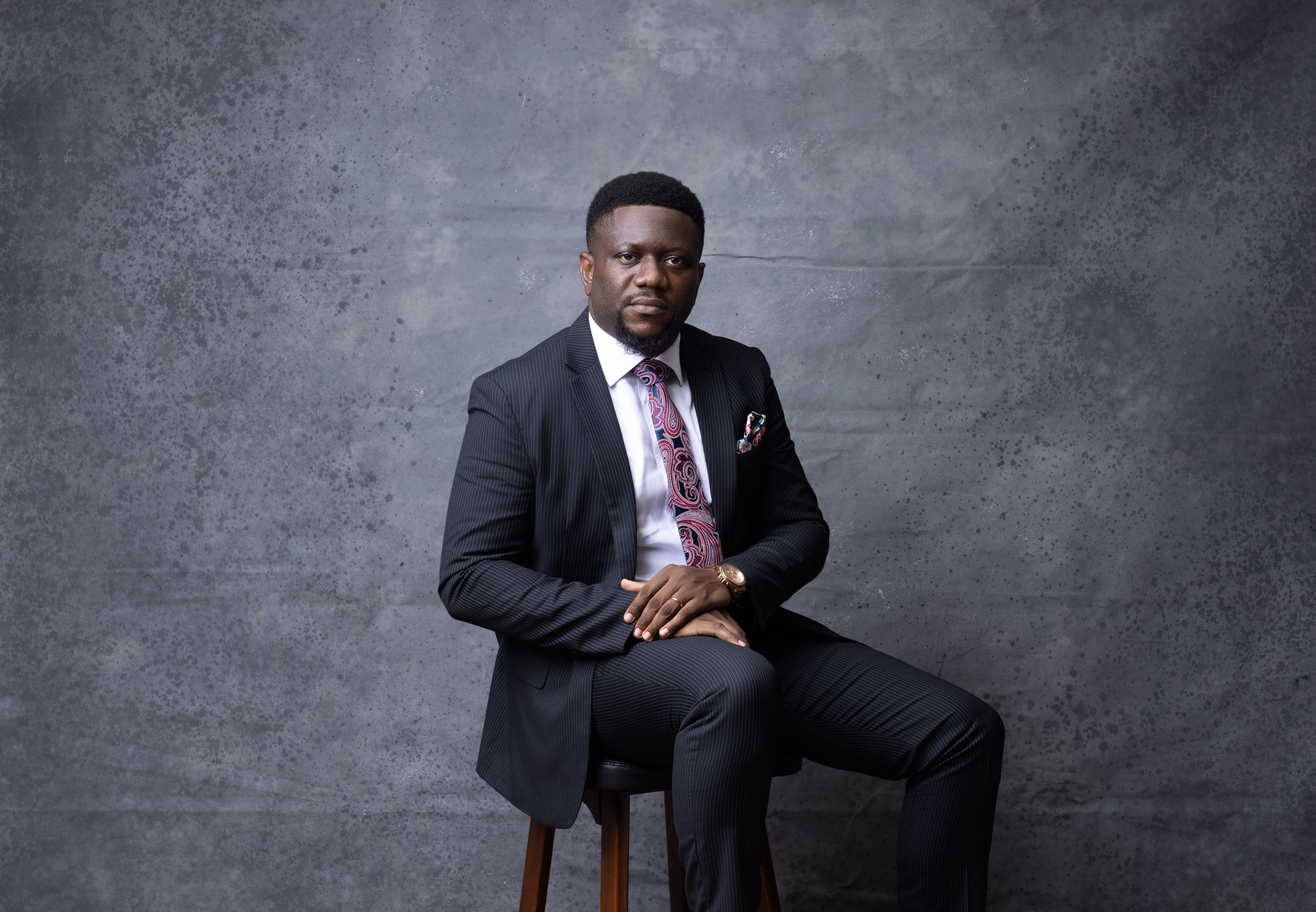 Seated portrait of person in business attire against textured gray background.