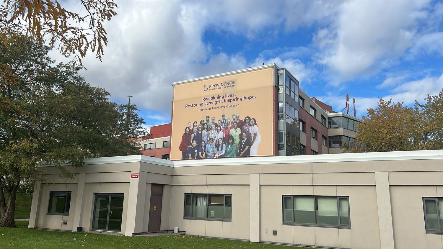 Modern building exterior with large mural of diverse group of people on upper facade.