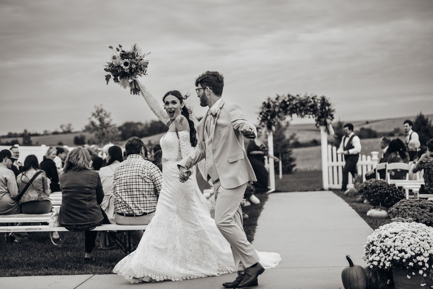 A black and white photograph of a bride and groom walking down the aisle at a wedding ceremony.