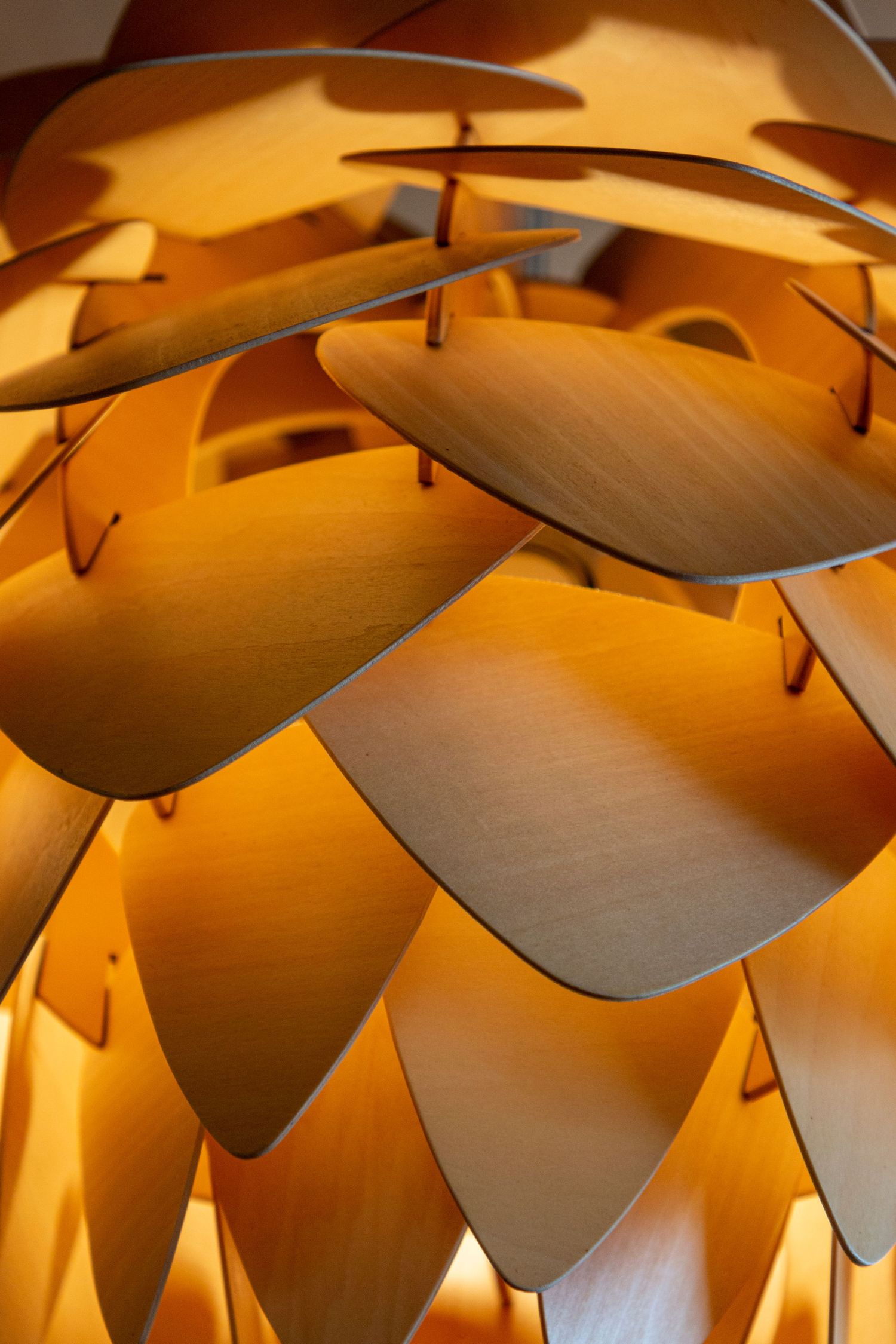 Close-up of a sculptural pendant light with layered, overlapping metallic leaves glowing in warm amber tones.
